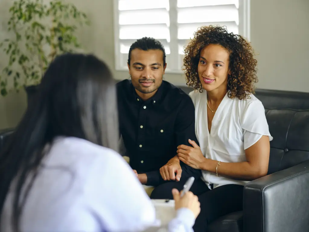 A couple sits close while listening to their therapist during a counseling session.