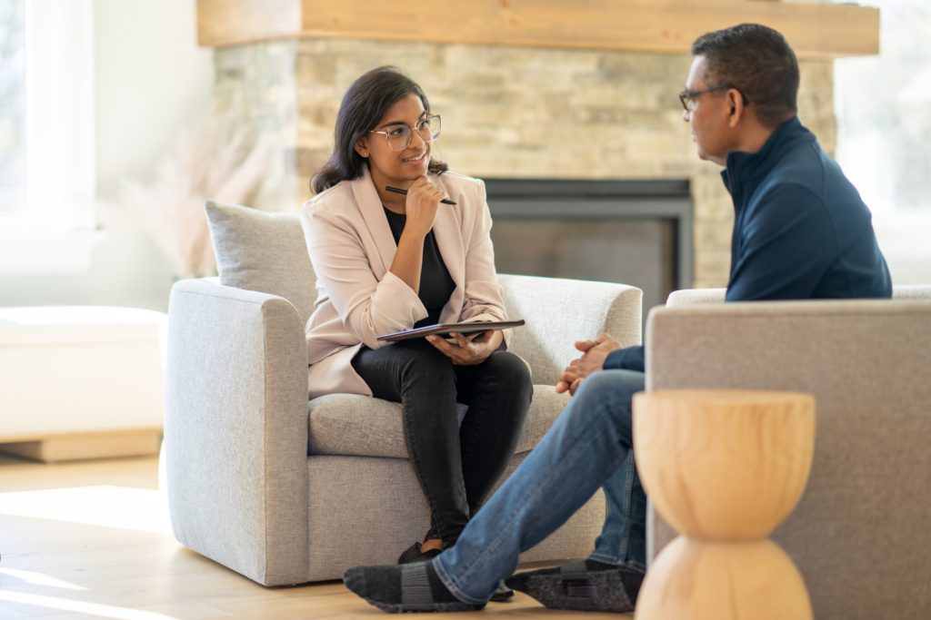 A psychiatrist looks toward her patient with interest while sitting in a comfortable office.