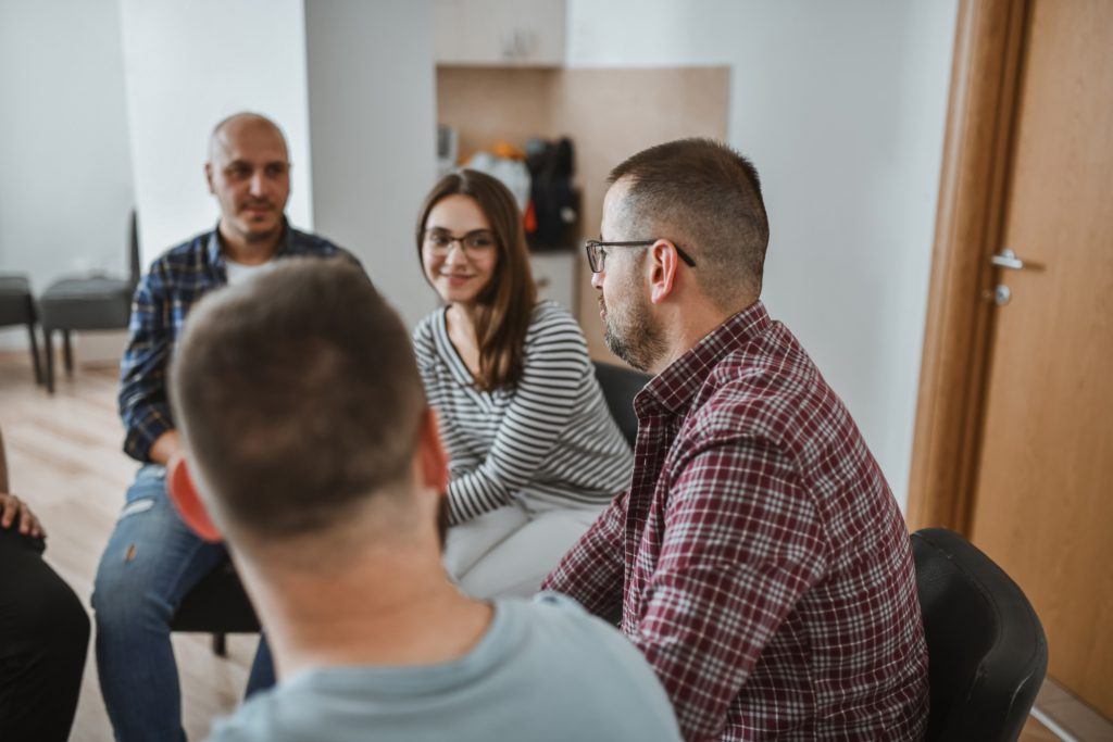 A small group of adults sit in a close circle during group therapy.