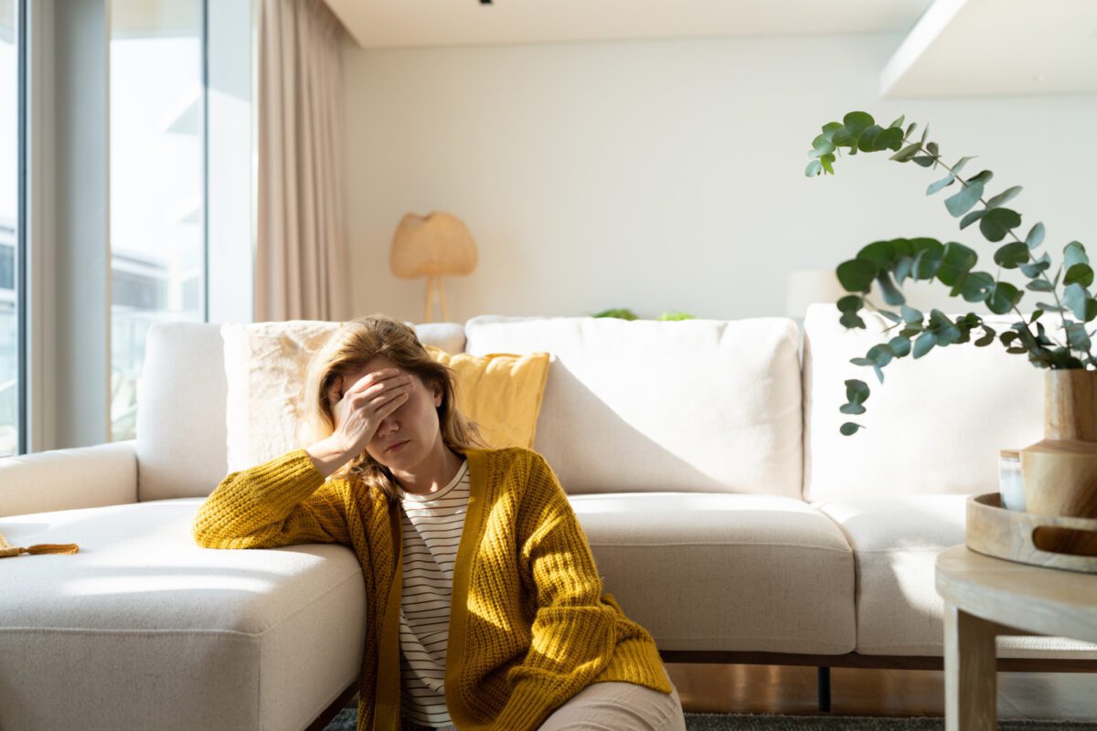 trauma-on-brain-1200×800 Frustrated woman holds her head in her hand as she sits on the floor in her living room