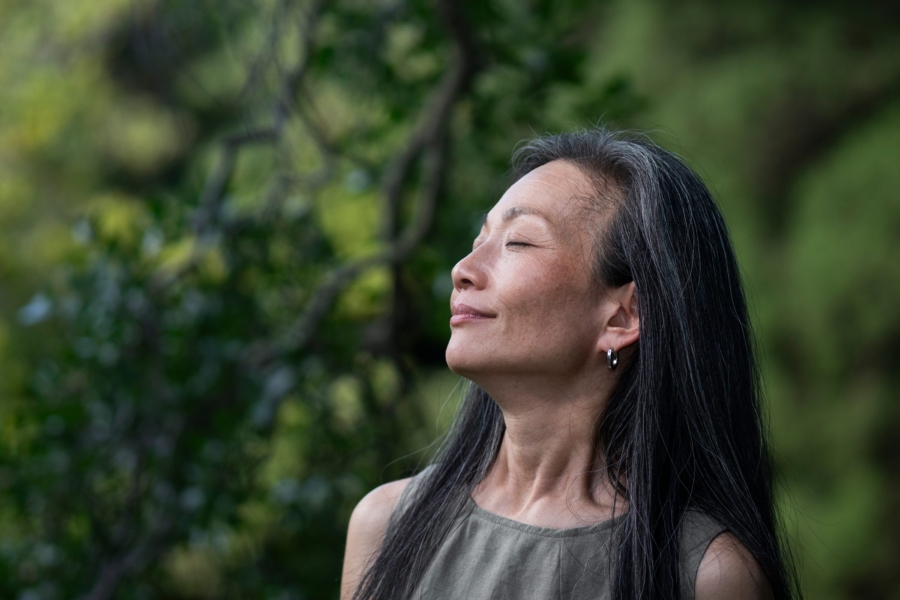middle-aged woman in sleeveless shirt smiling up at trees